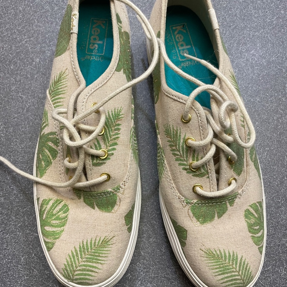 Unique Keds on platform with linen colored background and tropical leaf design
